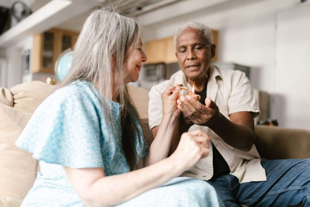 man helping woman light a blunt on the couch